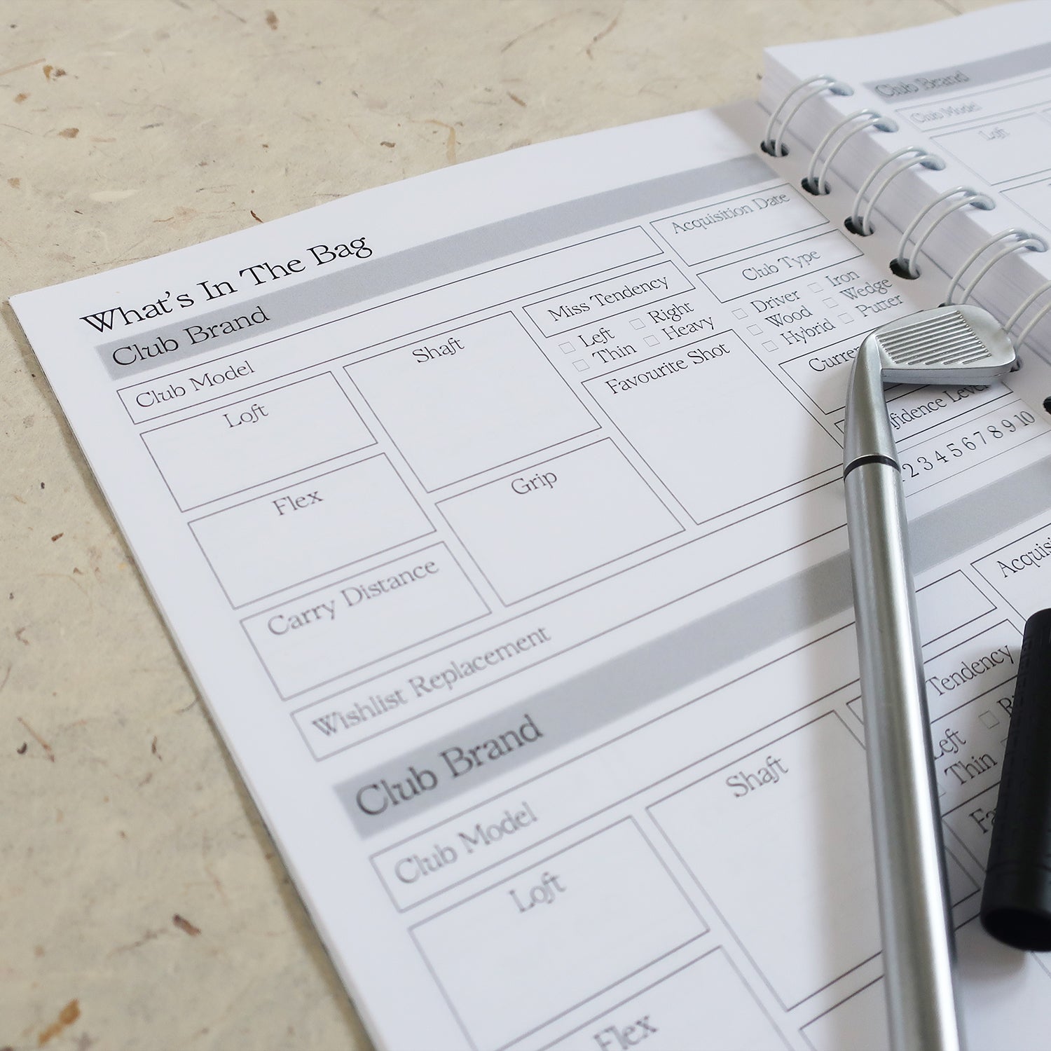 Golf Log Book Open On 'What's In The Bag' Page With A Golf Club Pen Laid Across It
