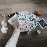 Collection of patterned pregnancy journals on a wooden desk with a hand holding one.