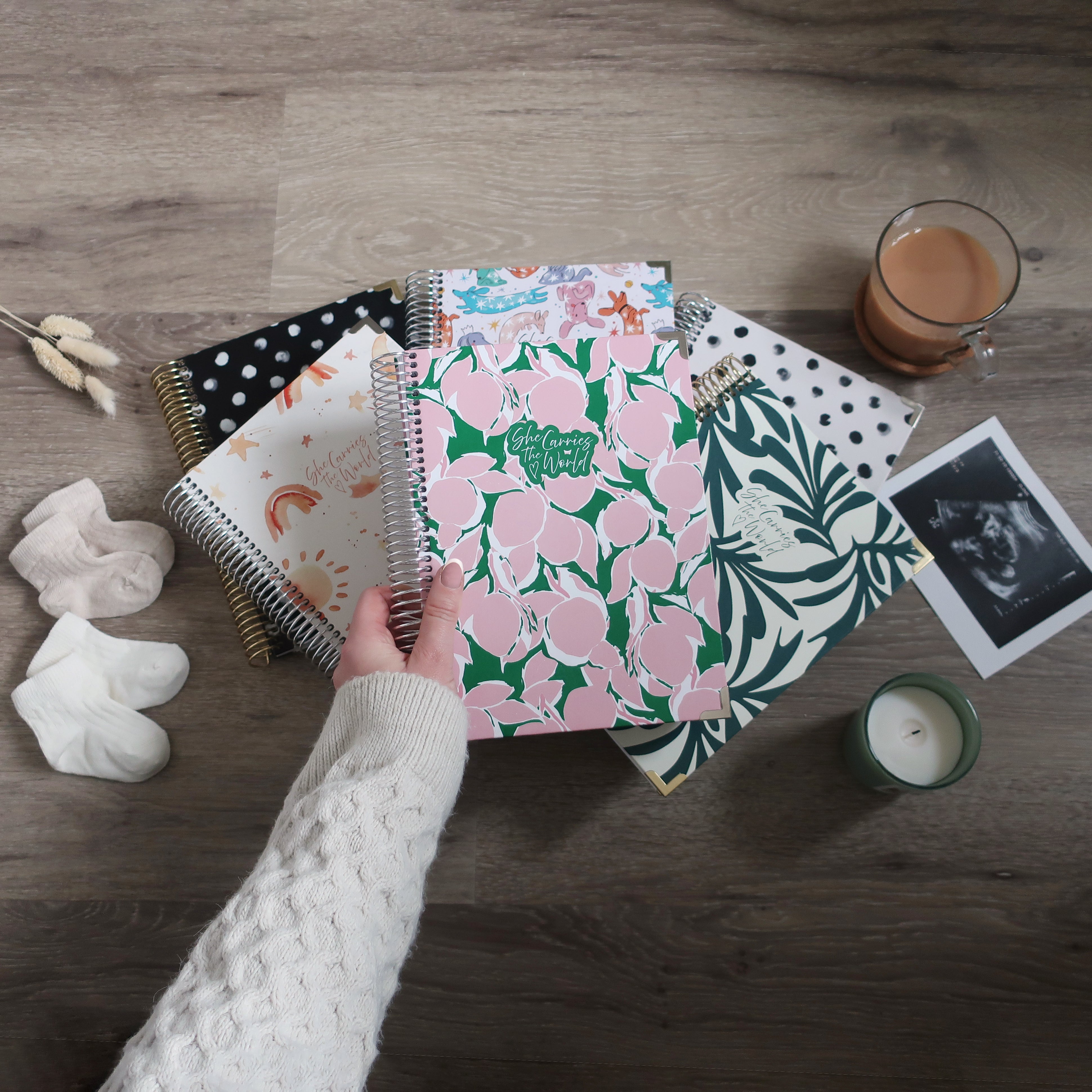 Collection of patterned pregnancy journals on a wooden desk with a hand holding one.