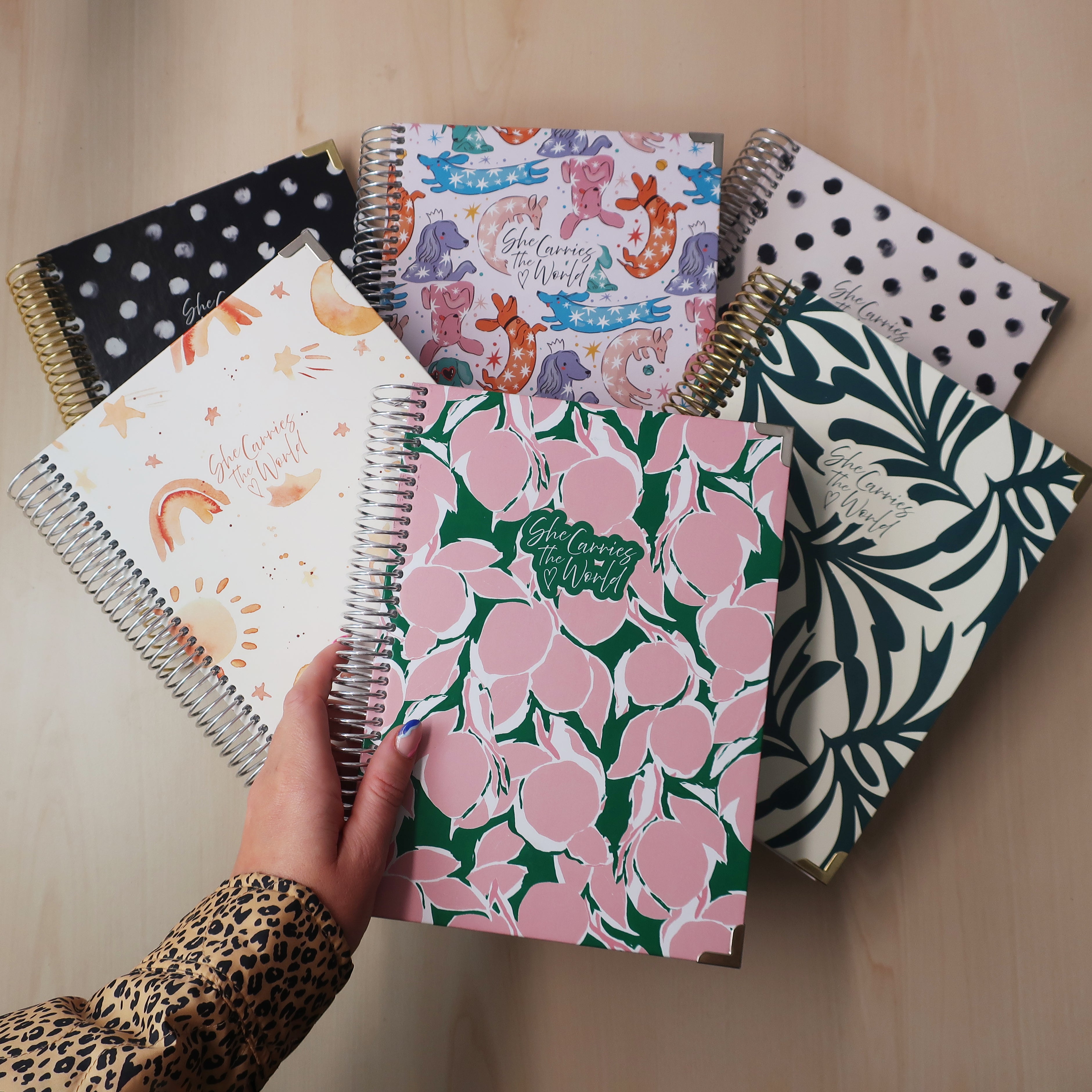 Collection of patterned pregnancy journals on a wooden desk with a hand holding one.