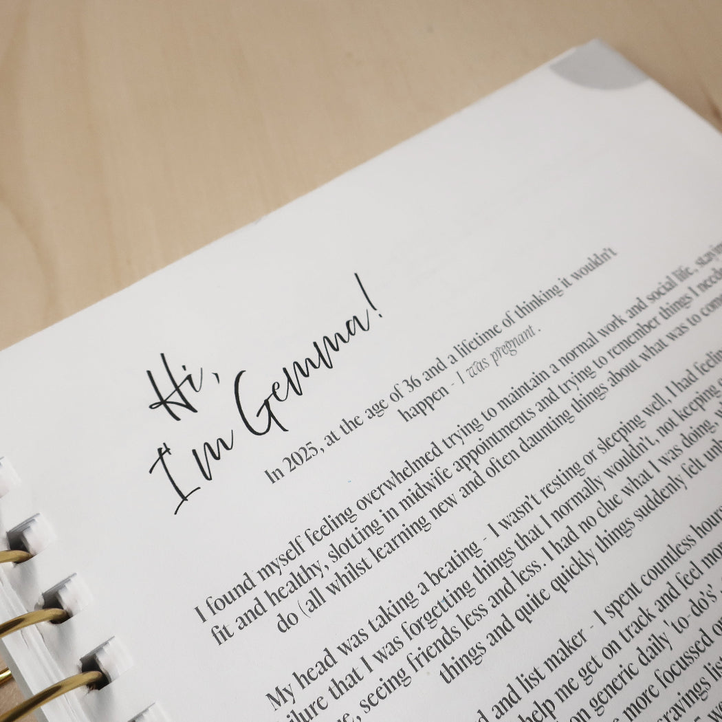 Opening page to 'She Carries The World' pregnancy journal on a wooden desk