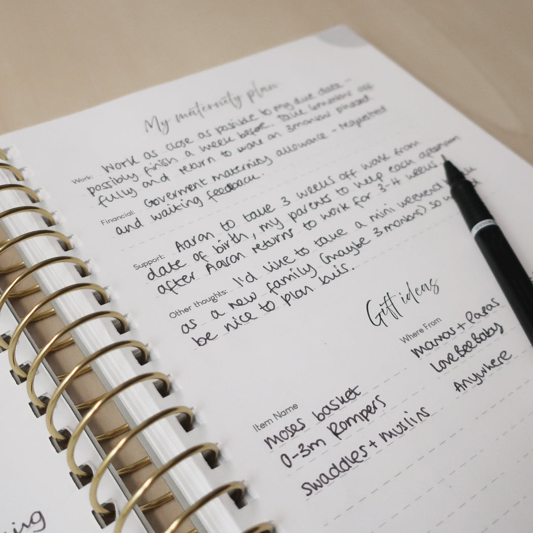 Open pregnancy journal with handwritten notes and a pen on a wooden desk