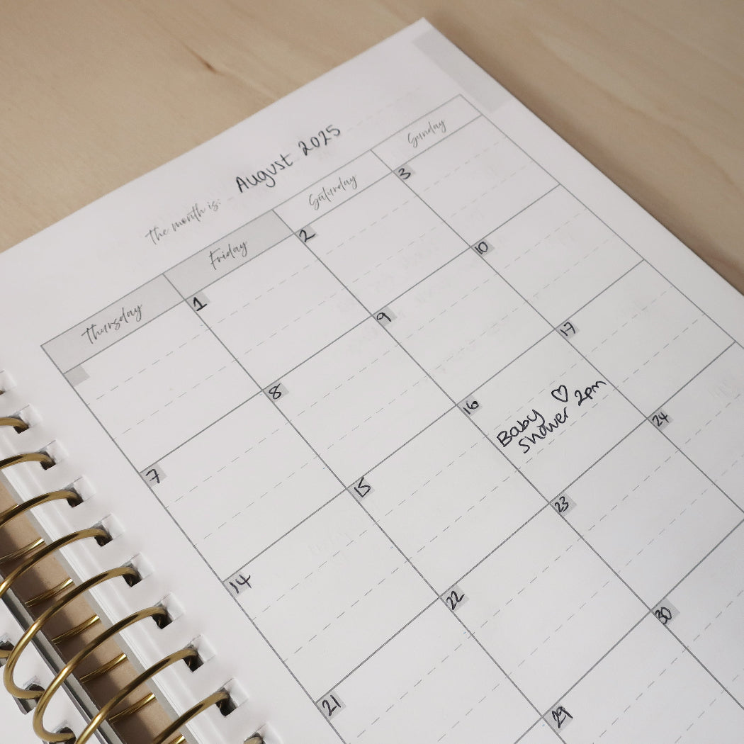 Calendar page in a pregnancy journal with handwritten note for 'baby shower' on a wooden desk