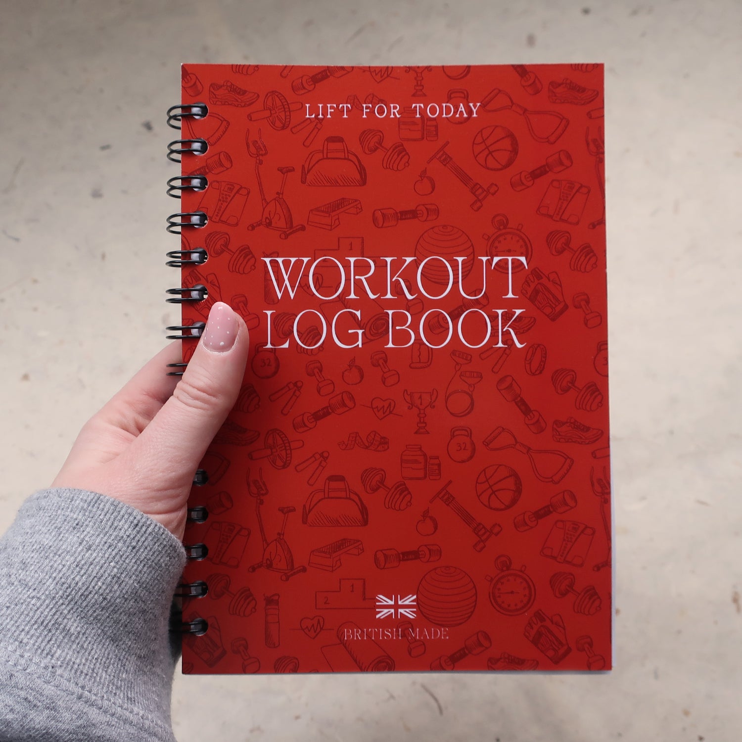 Orange workout log book held by a hand in a sports hoody on a light grey background