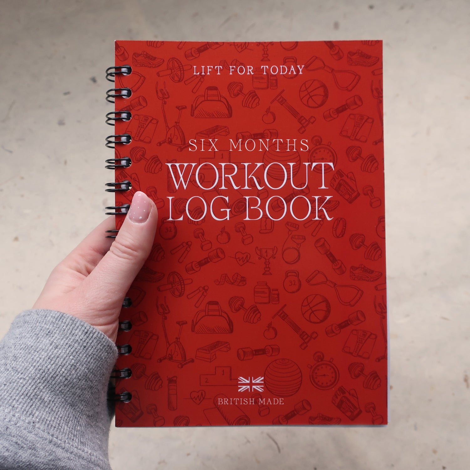 Orange workout log book held by a hand in a sports hoody on a light grey background