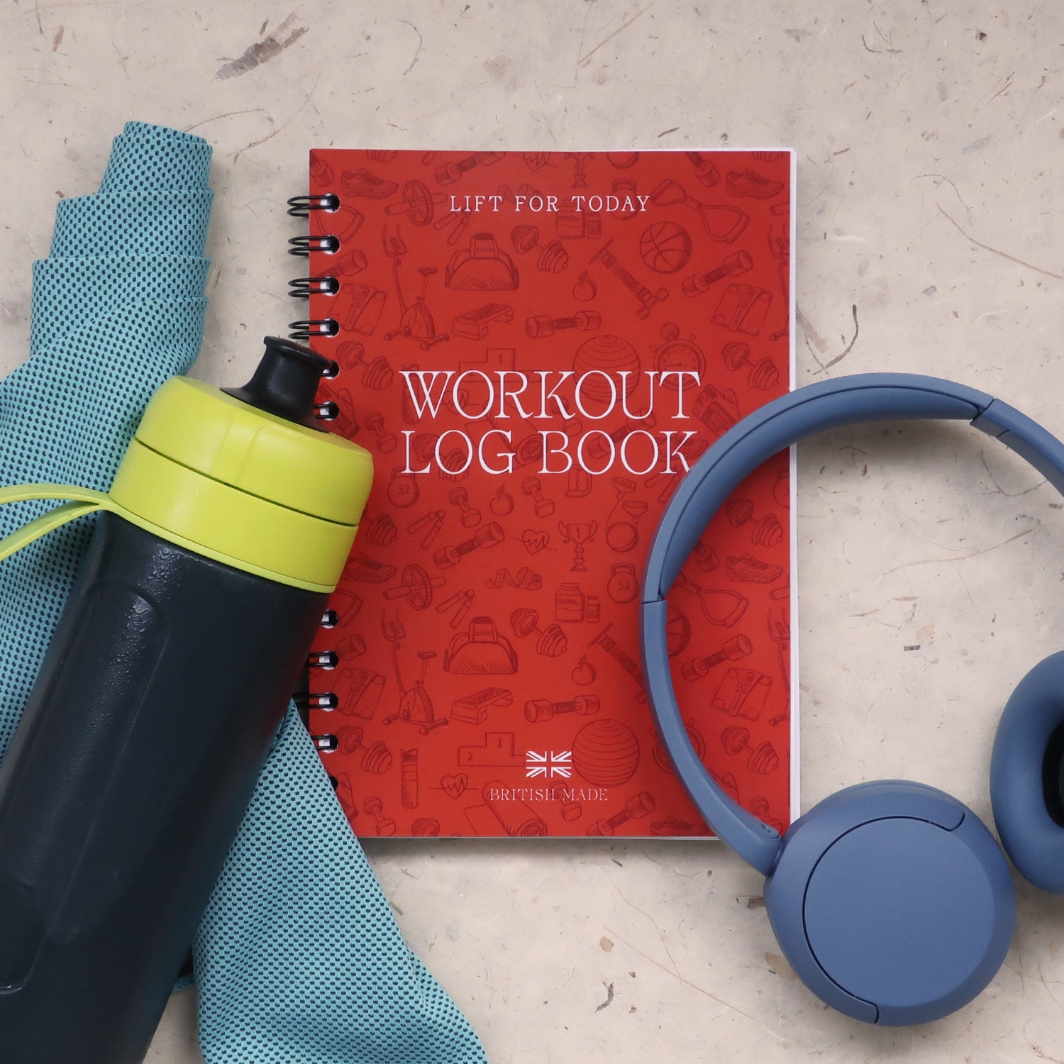 Orange workout log book with blue headphones, black water bottle, and blue towel on a textured surface