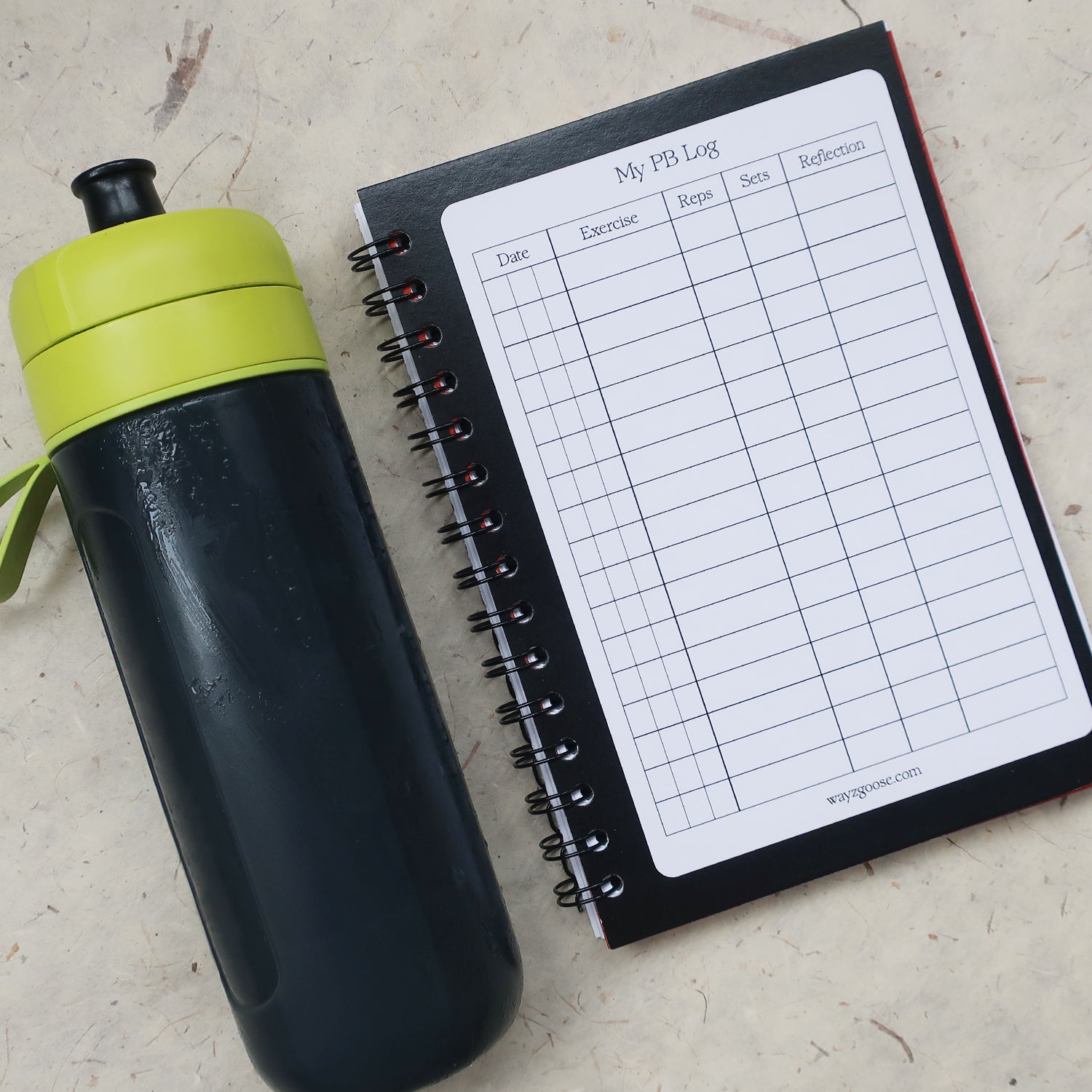 Black water bottle with green lid next to a workout log book, open on the Personal Best Log page