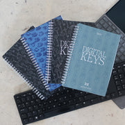 Address & Password Log Books | Four Printed Cover Designs Laid On Two Laptop Keyboards On A Neutral Background