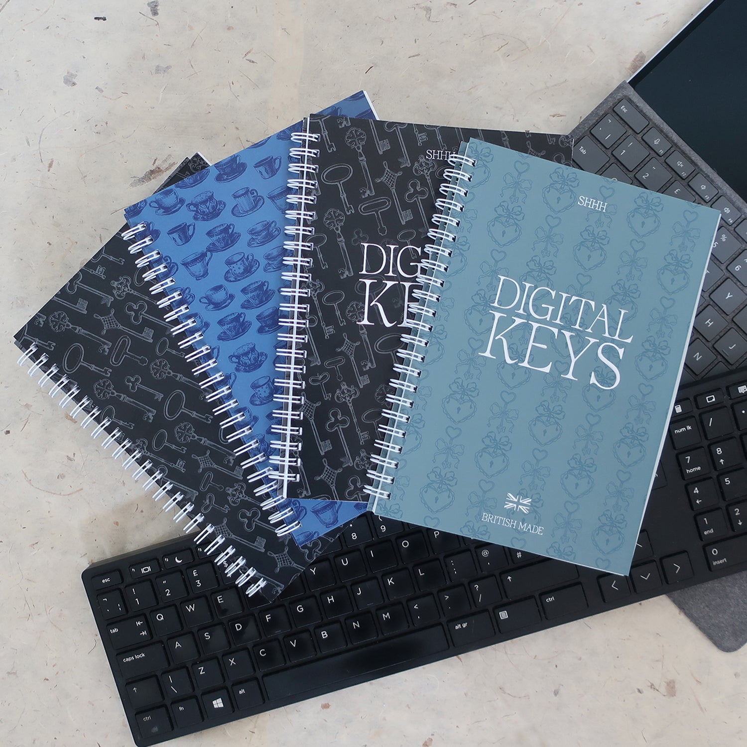 Address & Password Log Books | Four Printed Cover Designs Laid On Two Laptop Keyboards On A Neutral Background