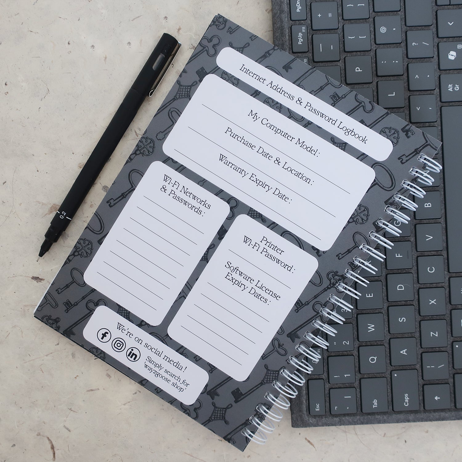 Address & password log book open on computer model information page with a pen and keyboard on a textured surface