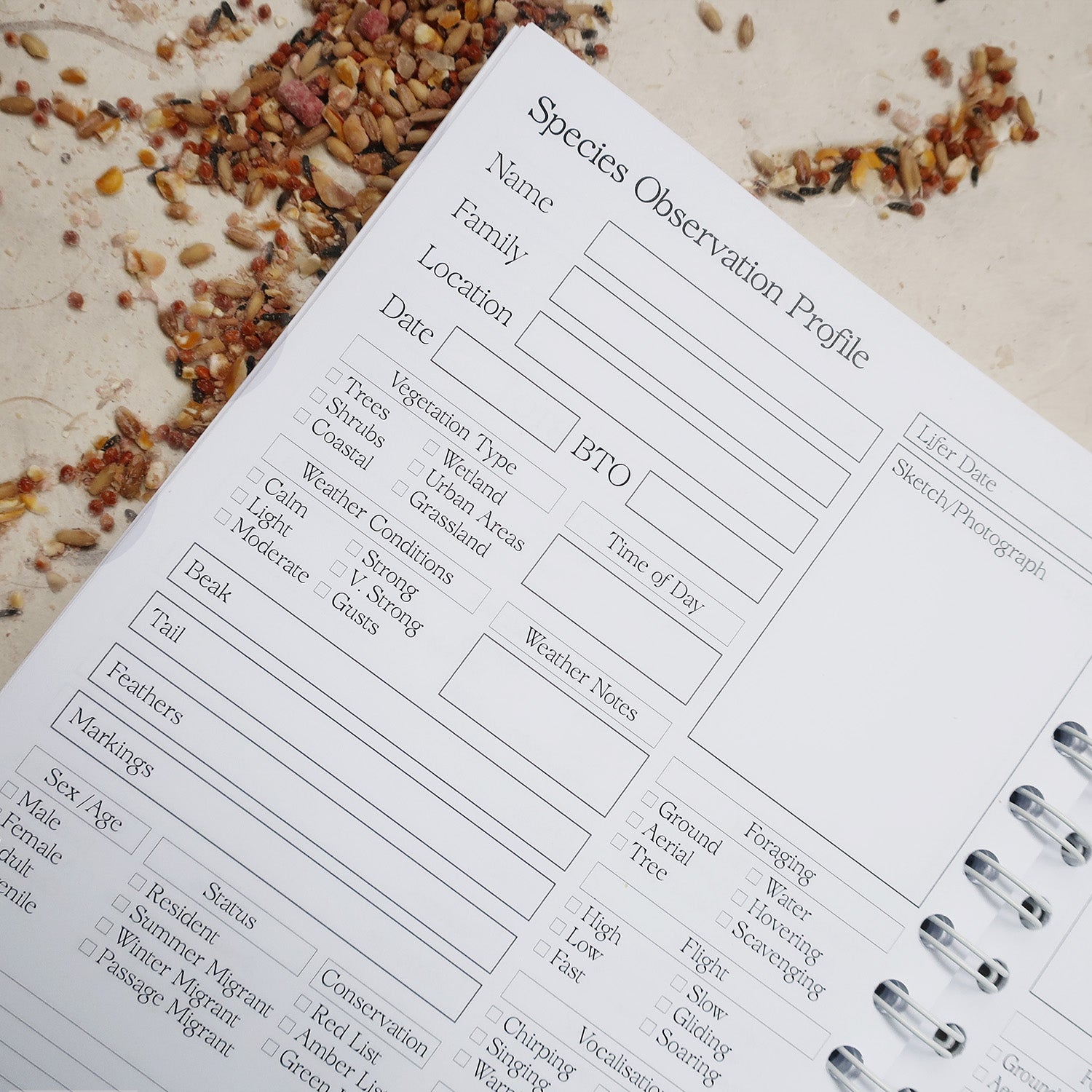 wayzgoose Bird Watching Log Book Open On The Species Observation Profile Page, Laid On A Textured Background With Bird Seeds