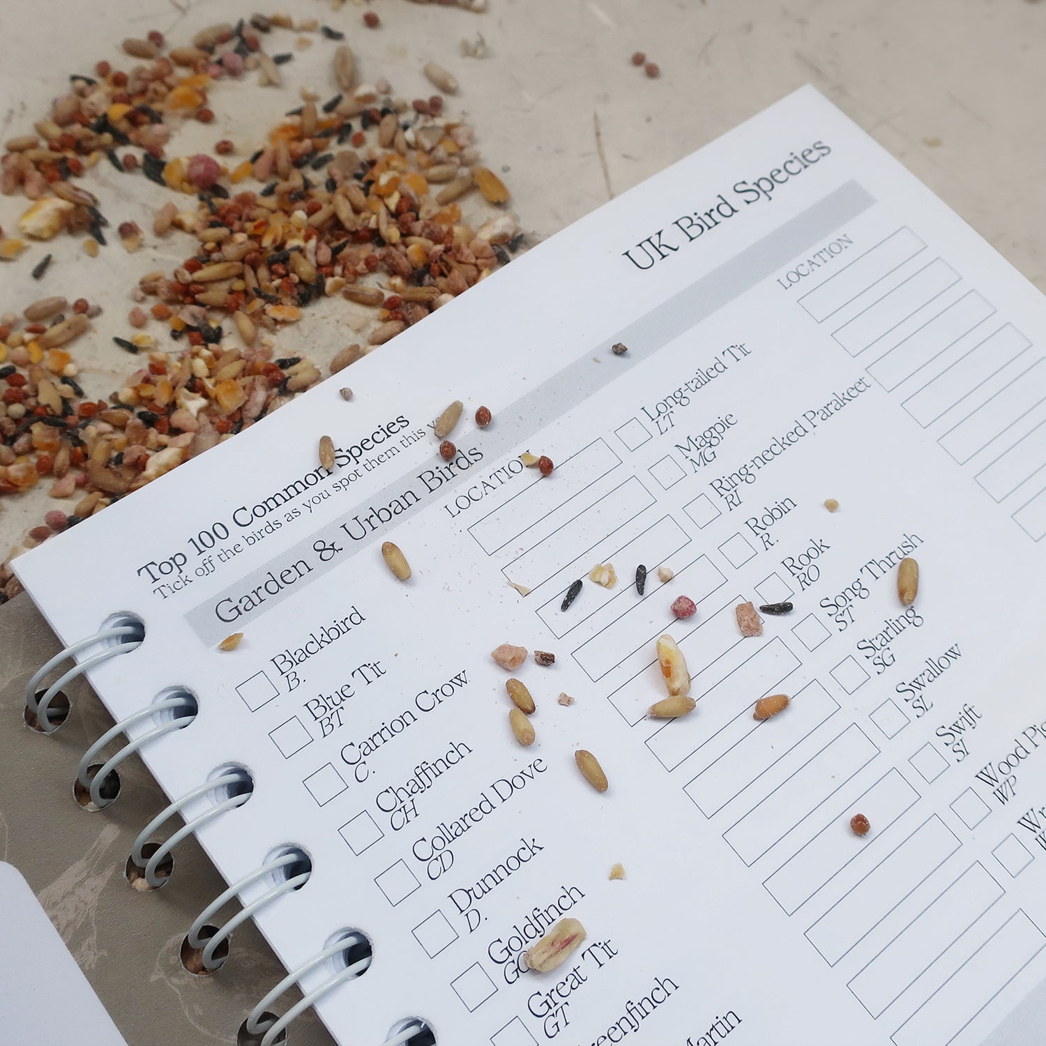 wayzgoose Bird Watching Log Book Open On The UK Bird Species Page, Laid On A Textured Background With Bird Seeds